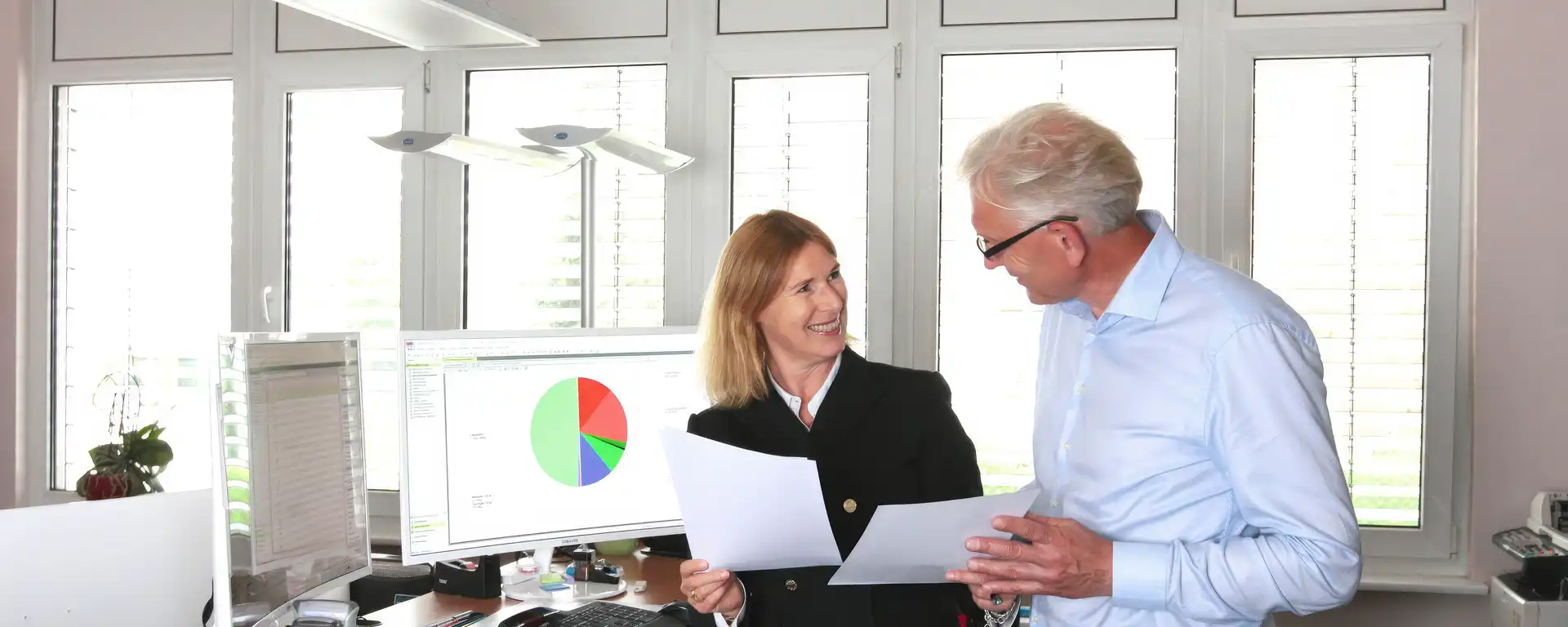 Frau und Mann stehen an einem Arbeitsplatz und unterhalten sich